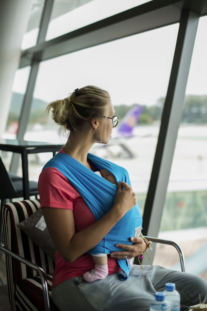A mother with her baby in a sling looks out the window at Phuket airport.